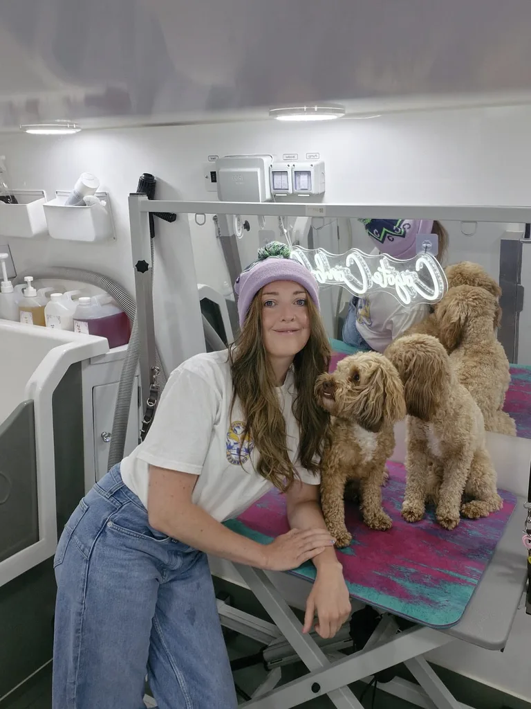 Carly posing with three freshly groomed dogs on the table, neon sign behind